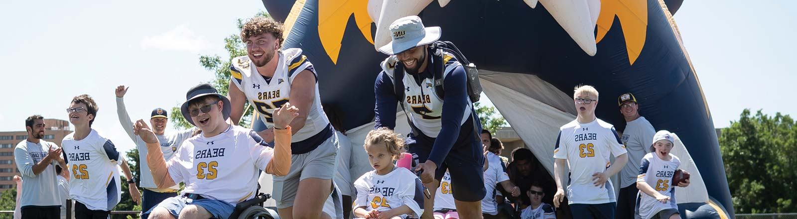 Student-athletes participating in the 'No Limits' camp, joyfully running onto the field with fellow camp participants.